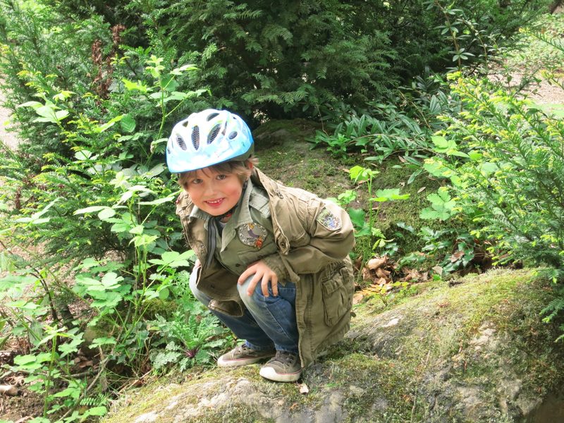 Merlin hockt mit Fahrradhelm im Grünen